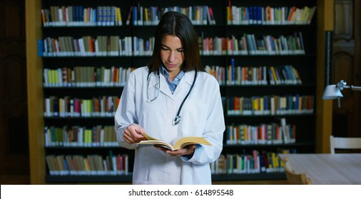 A Young And Beautiful Female Doctor In A Library Smiling Happy And Holding Books After Doing A Search And After Studying. Concept: Educational, Portrait, Library, And Medical Care And Welfare