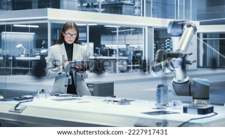 Young Beautiful Female Engineer Using a Tablet Computer, Researching and Developing a Futuristic Robotic Arm Machine in a High Tech Industrial Laboratory with Modern Equipment. Cinematic Footage.