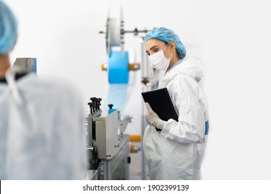 Young Beautiful Female Manager In Sterile Cloths Working In Face Mask Production Line Factory. Surgical Face Mask Production, Industry Factory And People Concept