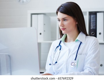 Young Beautiful Female Medicine Doctor  Sitting At The Table And Looking At Desktop Computer Screen.