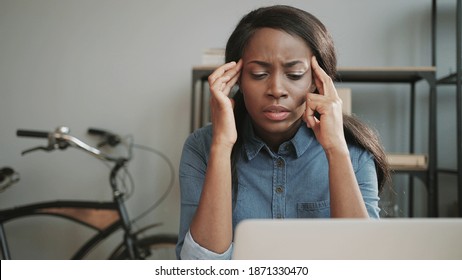 Young beautiful female office worker experiencing headache while sitting at work. Woman holds hands on temples. Fatigue and exhaustion from workload.
