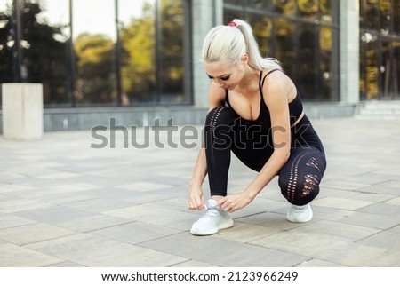 Young beautiful fit woman tying shoelaces of sneaker outdoors