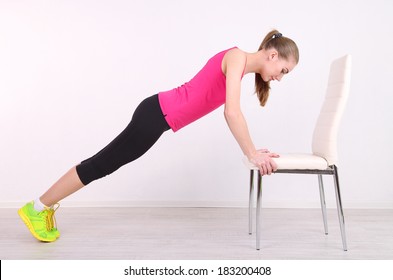 Young beautiful fitness girl exercising with chair in gym