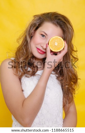 Young beautiful funny fashion model with orange slice on orange background. with makeup and hairstyle. holding lemon with nice smile.