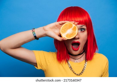 A Young Beautiful Funny Model With A Slice Of Orange Near Her Eyes, In The Background With Makeup, Hairstyle. Bright, Funny Summer Photo. Bright Background.