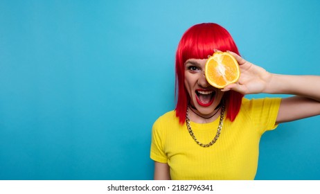 A Young Beautiful Funny Model With A Slice Of Orange Near Her Eyes, In The Background With Makeup, Hairstyle. Bright, Funny Summer Photo. Bright Background. A Place For Your Text.