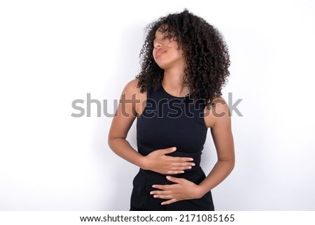 Young beautiful girl with afro hairstyle wearing black t-shirt over white background touches tummy, smiles gently, eating and satisfaction concept.