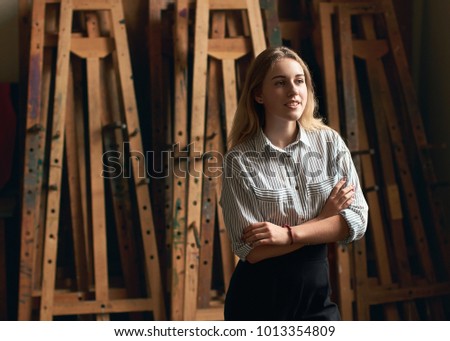 Young beautiful girl art or architecture student is dreaming of her future on old wooden easels background in studio