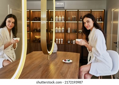 Young Beautiful Girl In A Beauty Salon In A White Coat Drink Coffe Near The Mirror. Bride's Morning Concept