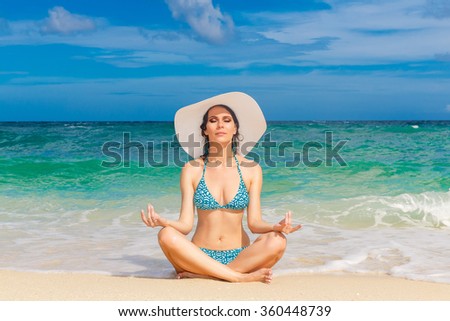 Young beautiful girl in bikini and straw white hat on the beach of a tropical island. Summer vacation concept.