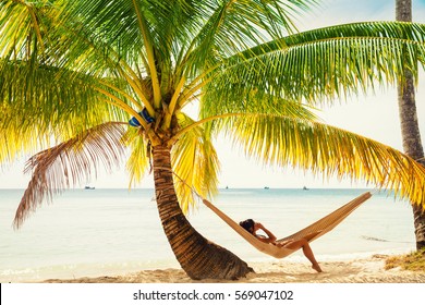 Young beautiful girl in black bathing suit with long black hair relaxing in hammock on the tropical beach on white background