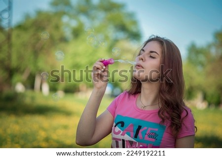 A young beautiful girl blows soap bubbles in nature.
