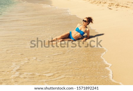 Young beautiful girl in a blue swimsuit lie in water on the beach