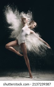 Young beautiful girl in a bodysuit in an explosion of white powder isolated on a dark black background. The concept of energy, power, movement. concept for advertising. 
