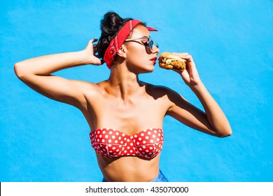 Young beautiful girl with a burger in her hands. Studio. Model. Fast food meal. The concept of food. handsome profile, sunglasses, a bandage on his head, a trendy makeup and hairstyle with horns