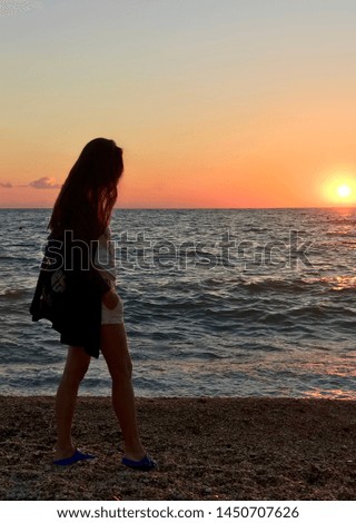 Young beautiful girl by the sea and the setting sun, calm water walks by the sea