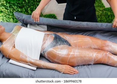 A Young Beautiful Girl Is Doing A Cosmetology Procedure Full Body Wrap In A Modern Beauty Salon. Spa Procedures In A Beauty Salon