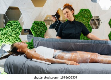 A Young Beautiful Girl Is Doing A Cosmetology Procedure Full Body Wrap In A Modern Beauty Salon. Spa Procedures In A Beauty Salon