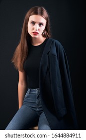 Young Beautiful Girl Dressed In A Black Jacket And Jeans Posing In Studio. Office Modern Style. Young Elegant Business Woman.