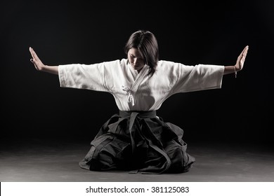 Young, beautiful girl dressed in hakama practicing Aikido in a dark gym