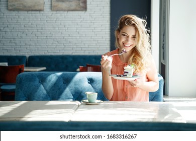 A young and beautiful girl eats sweets for breakfast in a cafe. A woman is eating a cake.