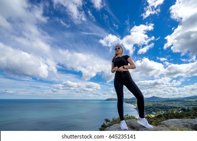 young beautiful girl female posing on top of the hill embracing nature with open arms sea clouds blue sky sport clothes