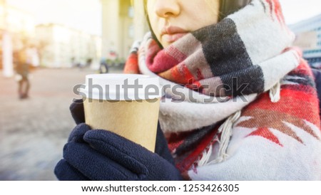 Young beautiful girl in gloves and in a large cozy scarf holding a paper cup of takeaway coffee in urban environment. Coffee to go in winter concept