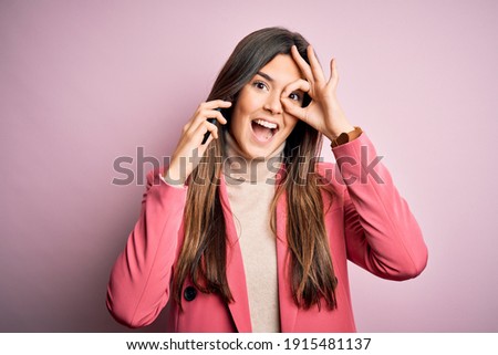 Young beautiful girl having conversation talking on the smartphone over white background with happy face smiling doing ok sign with hand on eye looking through fingers