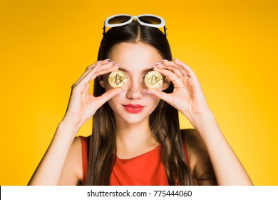 young beautiful girl holds golden bitcoins in hands and closes their eyes, on a yellow background
