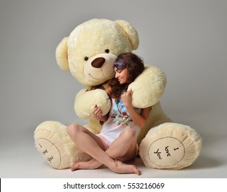 Young beautiful girl hug big teddy bear soft toy happy smiling on gray background