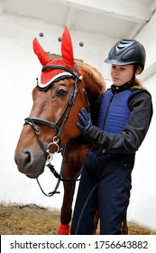 Young Beautiful Girl In A Jockey Outfit With Her Horse In Stable.