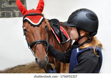 Young Beautiful Girl In A Jockey Outfit With Her Horse In Stable.