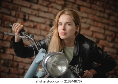 Young beautiful girl in the leather jacket is posing near the motorbike concept.