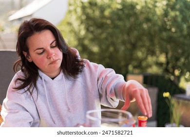 A young beautiful girl in a light hoodie enjoys life while sitting at a table on the terrace of her home. Dolce Vita concept - Powered by Shutterstock