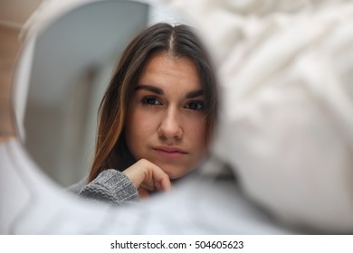 Young Beautiful Girl Looking In The Mirror, A Reflection Of The Different Emotions,white Bed In The Background