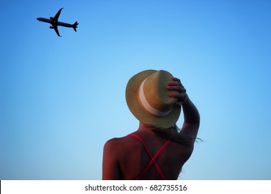 Young Beautiful Girl Looking Up At The Sky Where The Plane Is Flying Away