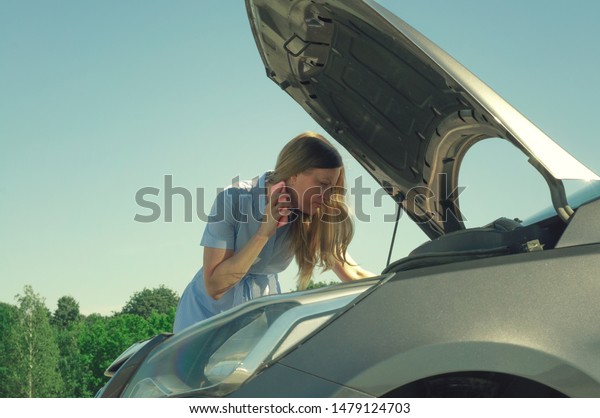 Young and\
beautiful girl near a broken car with an open hood. Problems with\
the car, does not start, does not\
work