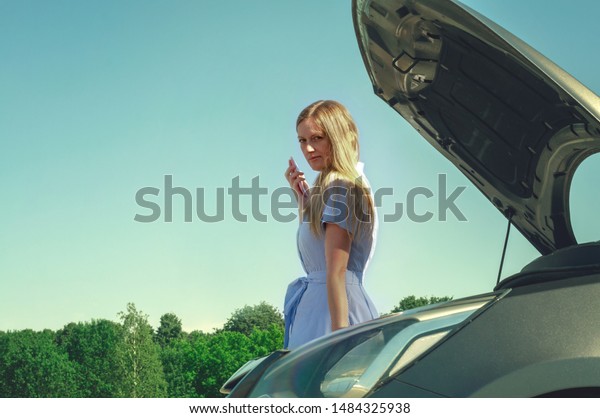 Young and\
beautiful girl near a broken car with an open hood. Problems with\
the car, does not start, does not\
work