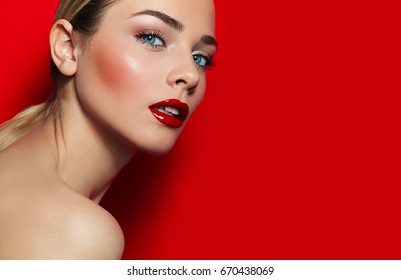 Young beautiful girl on red background in studio. Blue eyes, black eyelashes, red lips, white teeth. Well-groomed, luxurious. Hairstyle - tail, blonde, smooth skin. Beauty salon, fashion, dvertising.