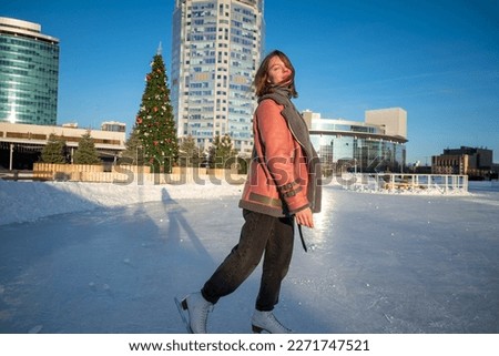a young beautiful girl on skates in a sheepskin coat on a skating rink against the backdrop of the metropolis and the rays of the sun