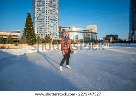 a young beautiful girl on skates in a sheepskin coat on a skating rink against the backdrop of the metropolis and the rays of the sun