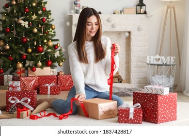 Young beautiful girl packing christmas gifts in decorated home interior
