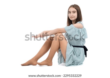 A young beautiful girl in a polka dot dress sits on the floor, isolated on a white background. High resolution photo. Full depth of field.