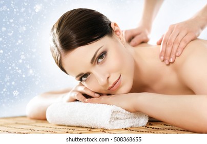 Young and beautiful girl relaxing in Christmas spa salon. Massage therapy over seasonal winter background with snowflakes. Healing medicine and health care concept. 