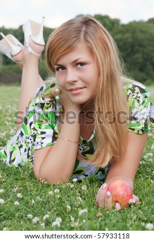 Young beautiful girl relaxing on the field with an apple in his hand