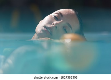 Young Beautiful Girl Relaxing In Pool With Floating Fruits. Half Underwater View Of Caucasian Model In Turquoise Water At SPA.