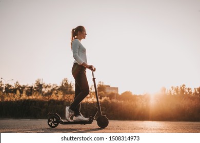Молодая красивая девушка катается на электрическом скутере летом на улице, против заката, есть свободное место для рекламы против неба