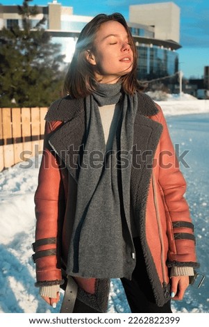 a young beautiful girl in a sheepskin coat on an ice rink against the backdrop of the metropolis and the rays of the sun