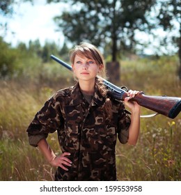 Young beautiful girl with a shotgun looks into the distance in an outdoor