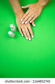 A young beautiful girl showing her tender hands with nice white or pastel pink manicured nails on a green background with 
nail polish bottles on it in a beauty salon.  - Shutterstock ID 1164852745